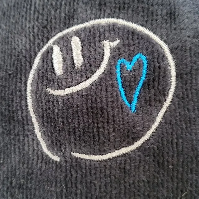 黒い布に白いスマイルと青いハートを刺繍した作品
